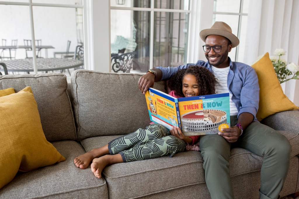 father and daughter reading book together on couch